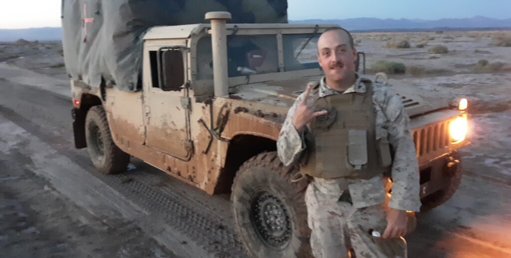 Picture of Dean Wetzel standing in front of high back military vehicle in uniform