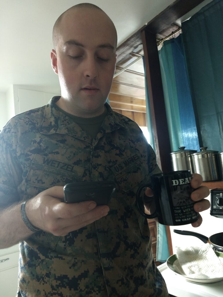 Picture of Dean Wetzel in his Marine Corps uniform drinking a cup of coffee and looking at his phone.