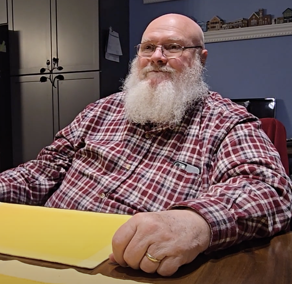 A picture of a United States Navy veteran, John Gooch. Sitting at a dinning table answering questions for the Veteran History Project.